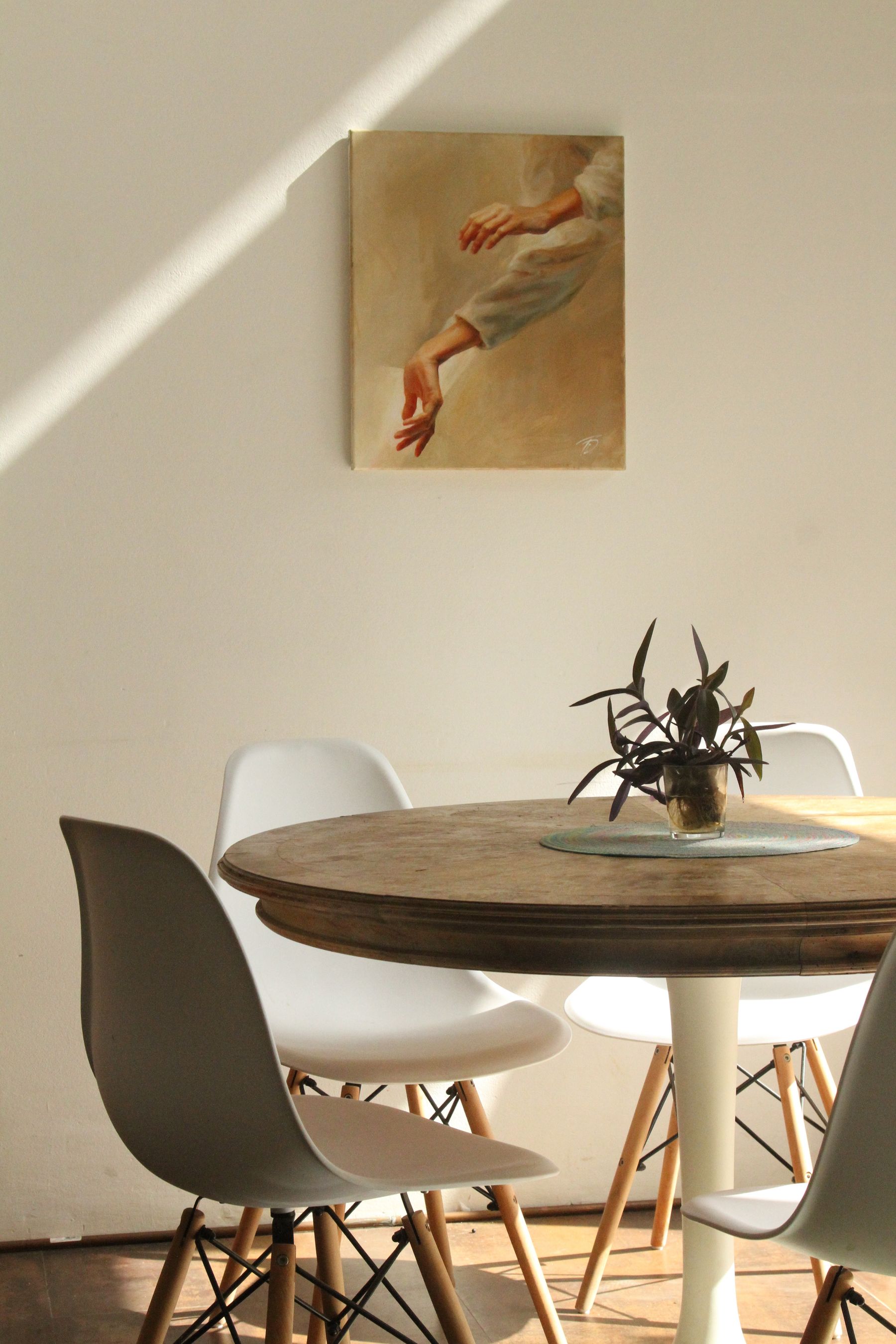 A round timber dining table with pale moulded chairs beside a white wall crossed by a blade of sunlight.