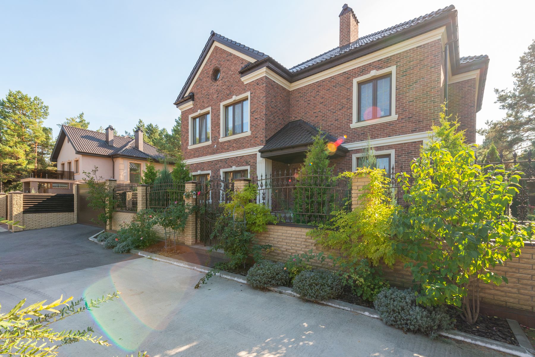 A two-storey brick house with a tiled roof, a driveway and established planting, photographed in late afternoon light.