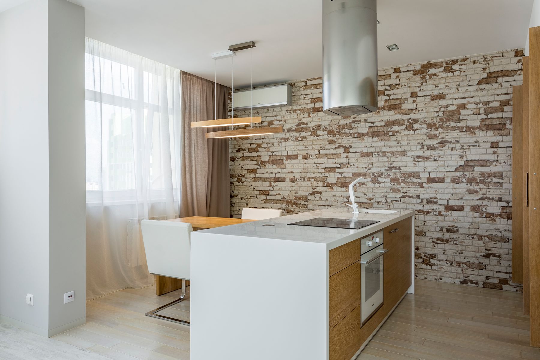 A white kitchen island with an integrated hob, set against an exposed brick wall and timber cabinetry.
