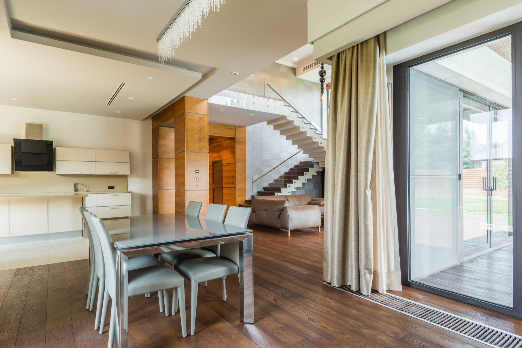 An open-plan dining and kitchen area with timber flooring, a staircase behind, and sliding glass doors open to a deck.