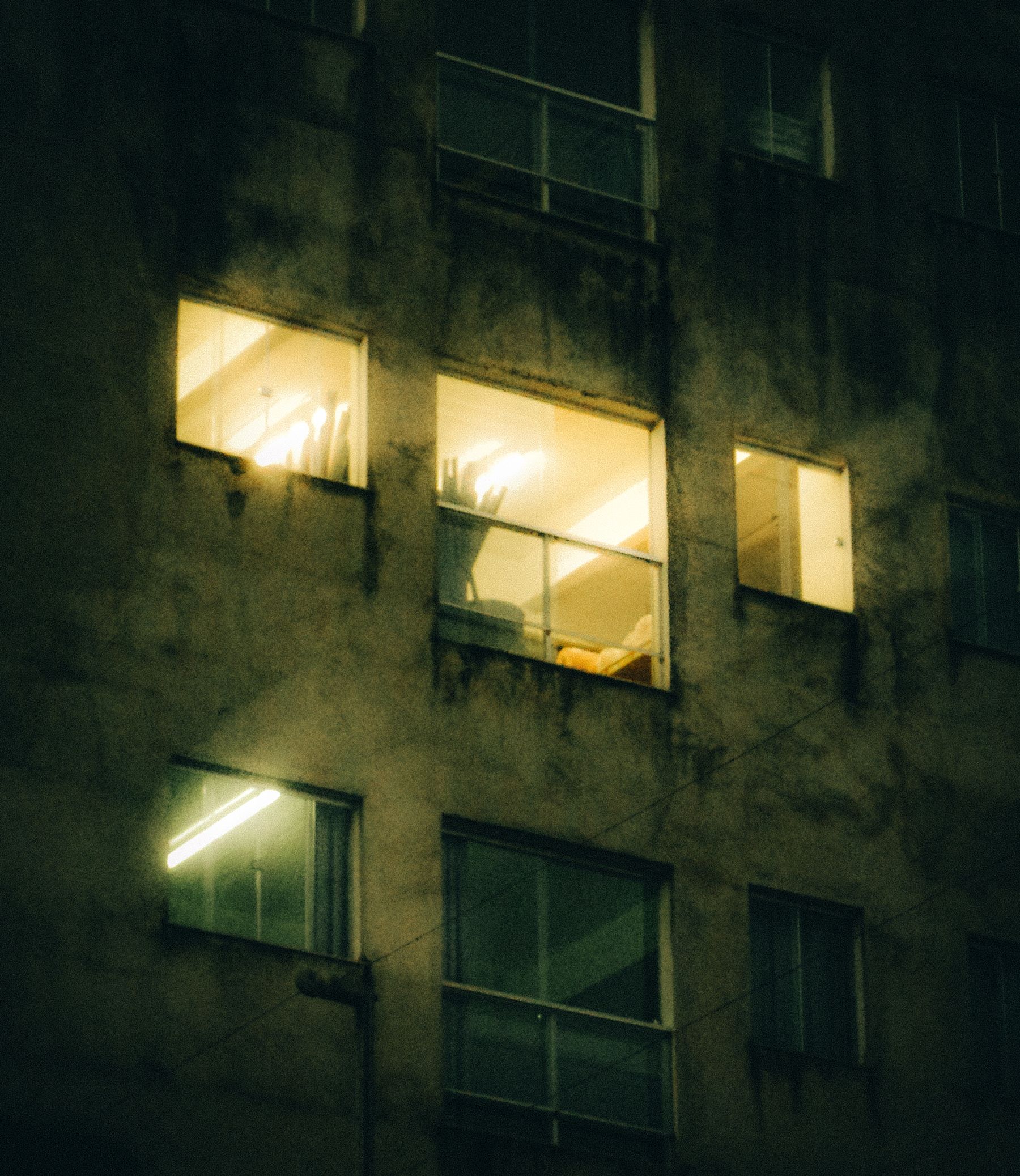 A residential building at night with warm lit windows glowing against a dark concrete facade.